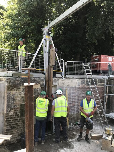 workers in high vis stood in drained canal, using a gantry to carry out repairs 